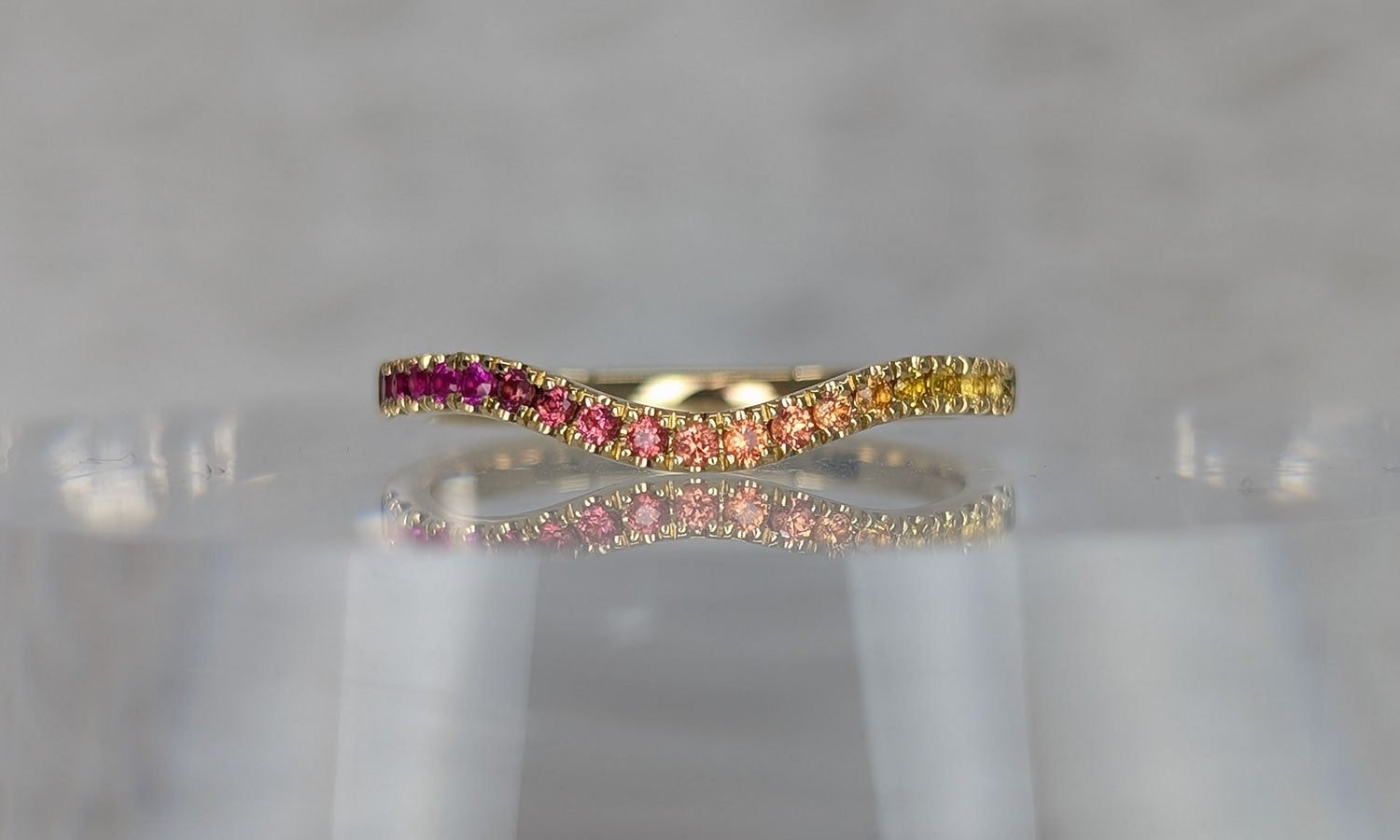 Custom curved sapphire wedding band with pink, orange and yellow gemstones set in textured yellow gold