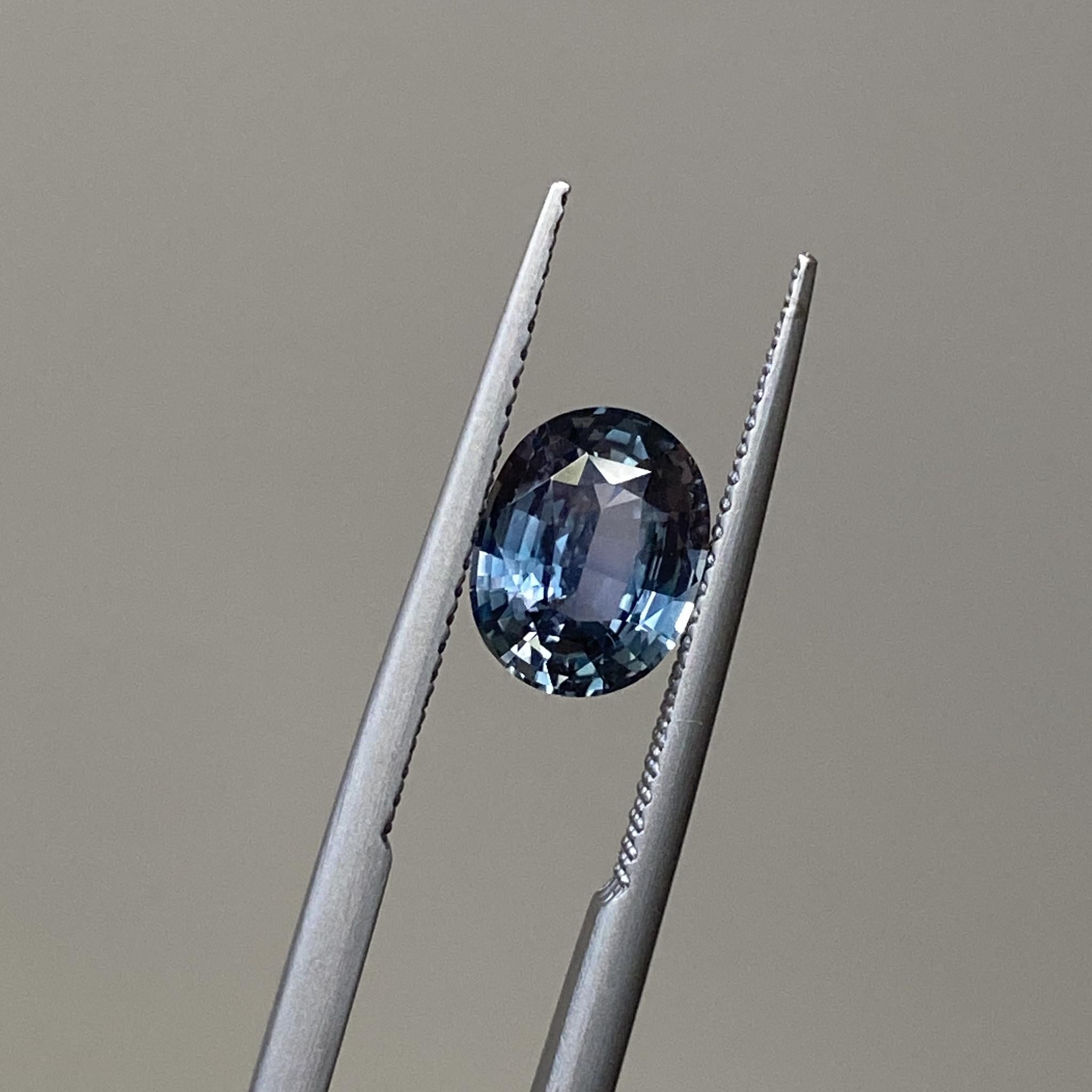 Close-up of the steel blue and silver sapphire, emphasizing its intricate color shifts and polished oval cut.