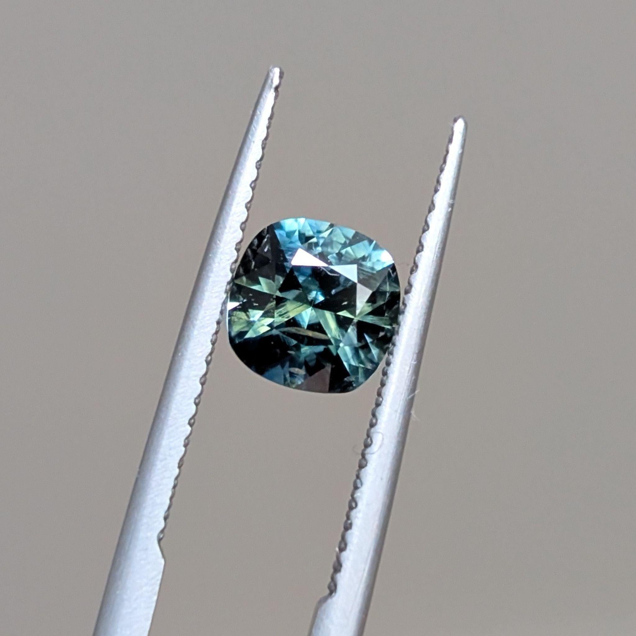 Close-up of High Tide sapphire – Cushion-cut 1.38ct sapphire held in tweezers, with deep oceanic colour zoning
